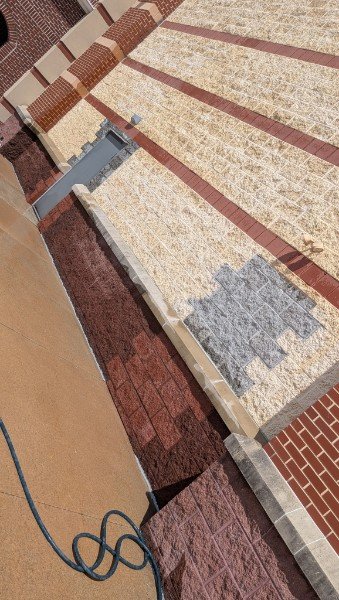 Angled view along the wall showing the new gray block toothed into the tan split-face wall and the rebuilt burgundy base and cap at the old door location, York County PA