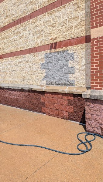 Old door opening in a commercial split-face block wall filled in with new gray block toothed into the tan wall, with a rebuilt burgundy base course and cap stone, York County PA