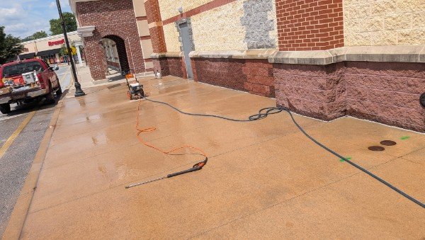 Wide view of a retail building wall after masonry work, with the sidewalk being pressure washed and the filled-in opening visible down the wall, York County PA