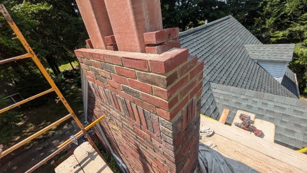 New brick courses laid around two clay flue liners at the top of a chimney, with the decorative band reproduced, York County PA