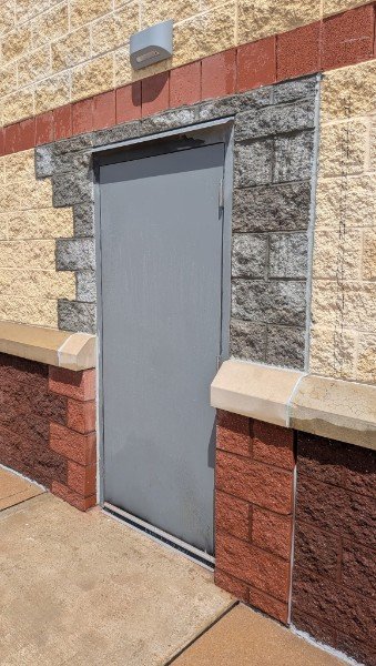 New opening cut into a tan split-face block wall with a gray commercial steel door installed, new block jambs and burgundy base with cap stones on both sides, York County PA